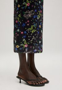 Bloemen midi rok met een donkere achtergrond, versierd met kleurrijke wilde bloemen. Gecombineerd met zwarte strap sandalen en een gladde, donkere huid.