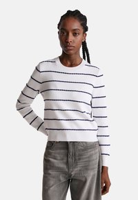Biały sweter z dzianiny z granatowymi poziomymi paskami, okrągłym dekoltem, prążkowanymi mankietami i dołem. Zestawiony z szarymi dżinsami. Gładka tekstura.