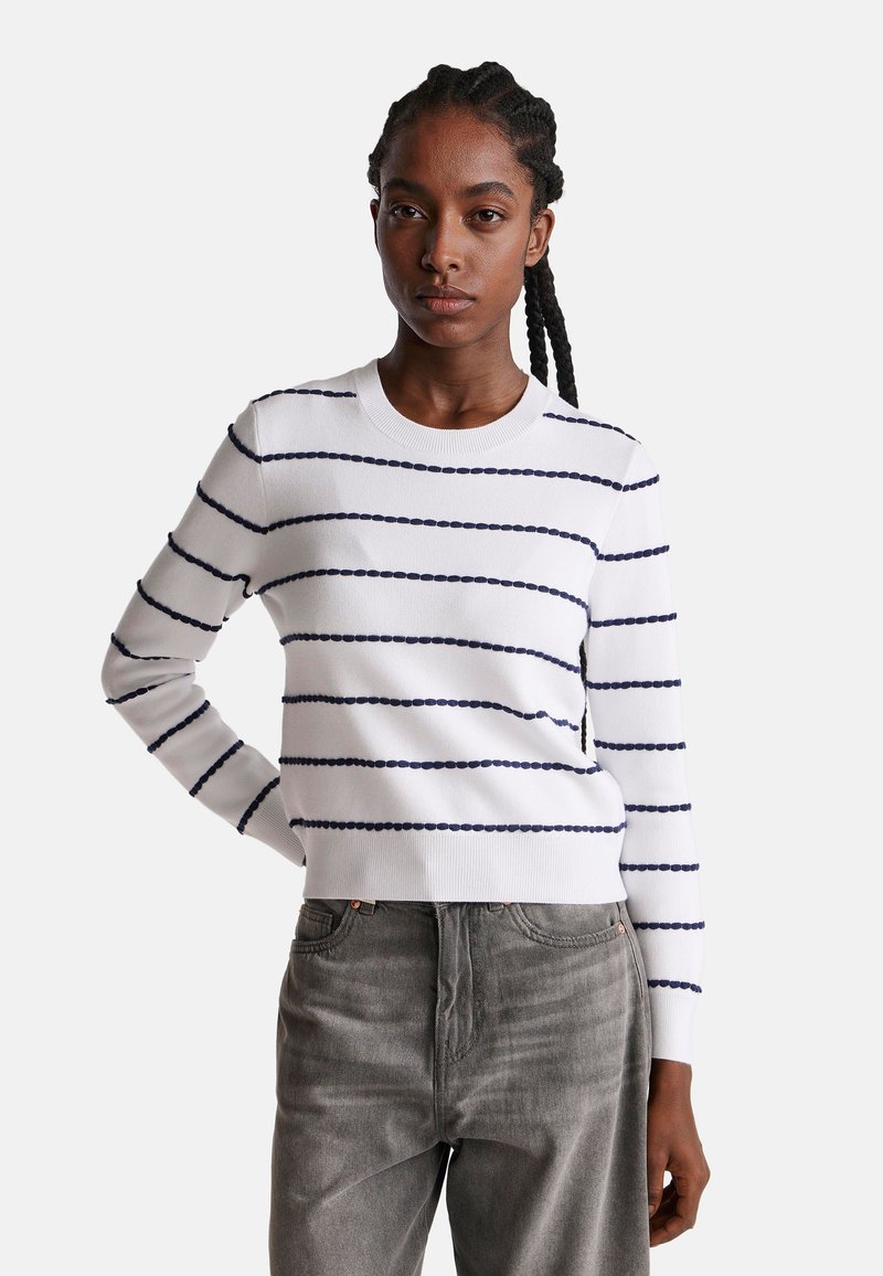 Biały sweter z dzianiny z granatowymi poziomymi paskami, okrągłym dekoltem, prążkowanymi mankietami i dołem. Zestawiony z szarymi dżinsami. Gładka tekstura.