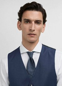 Gilet texturé bleu marine sur une chemise blanche, accentué par une cravate à motifs avec de petits cercles. Détails de col net visibles.