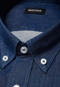 Granatowa koszula z dżinsu z kołnierzykiem typu button-down, przezroczystymi guzikami z wzorem krzyża i kontrastowym wykończeniem kołnierzyka od wewnątrz.