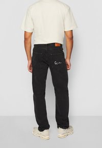Black denim jeans with a straight cut, featuring two back pockets, a leather tag, and white embroidered detail on one pocket.