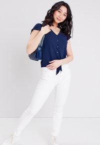 Marineblause mit kurzen Ärmeln und einem Band in der Taille, kombiniert mit weißen Skinny-Jeans und weißen Sneakers. Strukturierter Stoff, lässiger Look.