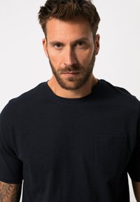 Maglietta in cotone blu navy con collo giro e maniche corte. Presenta una piccola tasca sul petto e una consistenza liscia e morbida.