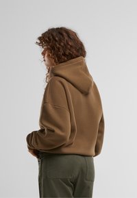 Braun kapuzenpullover mit lockerer Passform, cropped Design und gerippten Bündchen, kombiniert mit olivgrünen Hosen. Weicher Stoff mit minimalen Details.