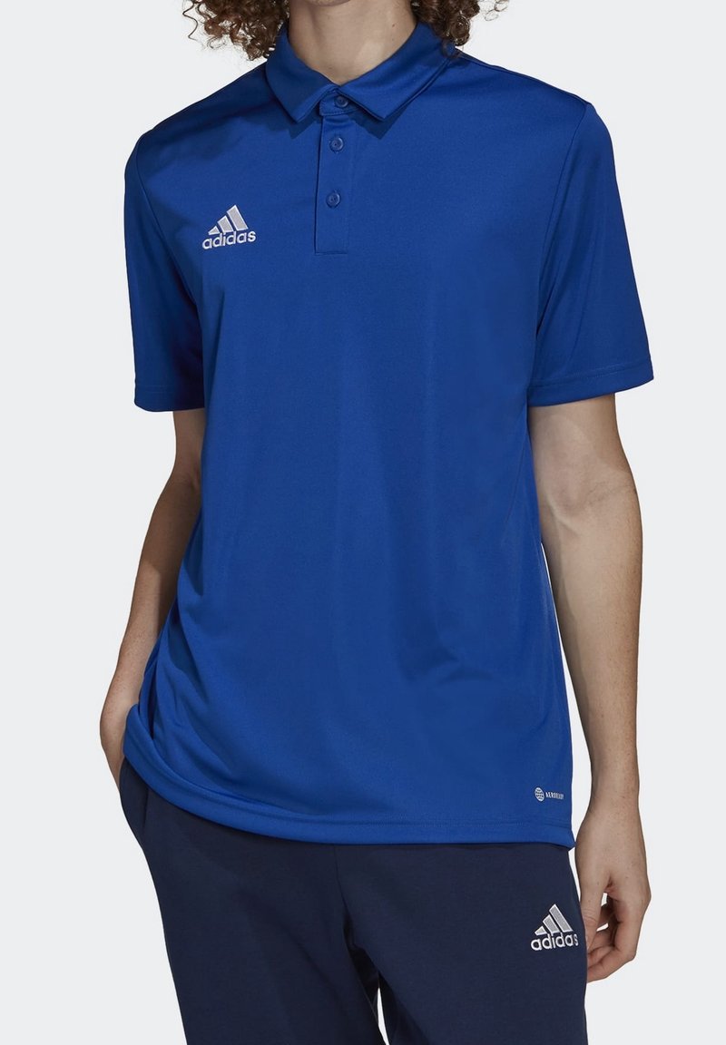 Polo bleu en tissu lisse avec col, trois boutons et logo Adidas blanc sur la poitrine gauche. Assorti à un pantalon bleu marine.