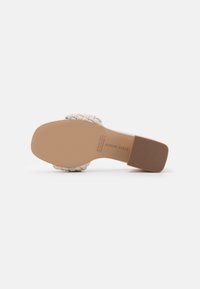 Sandale beige à talon bloc bas, bout carré, bride tressée et semelle marron lisse avec détails de marque et de taille.