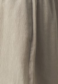 Tissu beige froissé avec une surface texturée, présentant des lignes verticales étroites. Le matériau semble doux et léger.