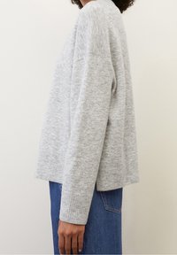 Maglione lavorato a maglia di un grigio chiaro con una vestibilità rilassata, orlo e polsini a coste, con una vista laterale che mette in evidenza la sua silhouette ampia e la texture.