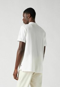 Vit polo skjorta i mjukt material. Har korta ärmar, krage och sidöppningar. Minimalistisk design med en liten logodetalj.