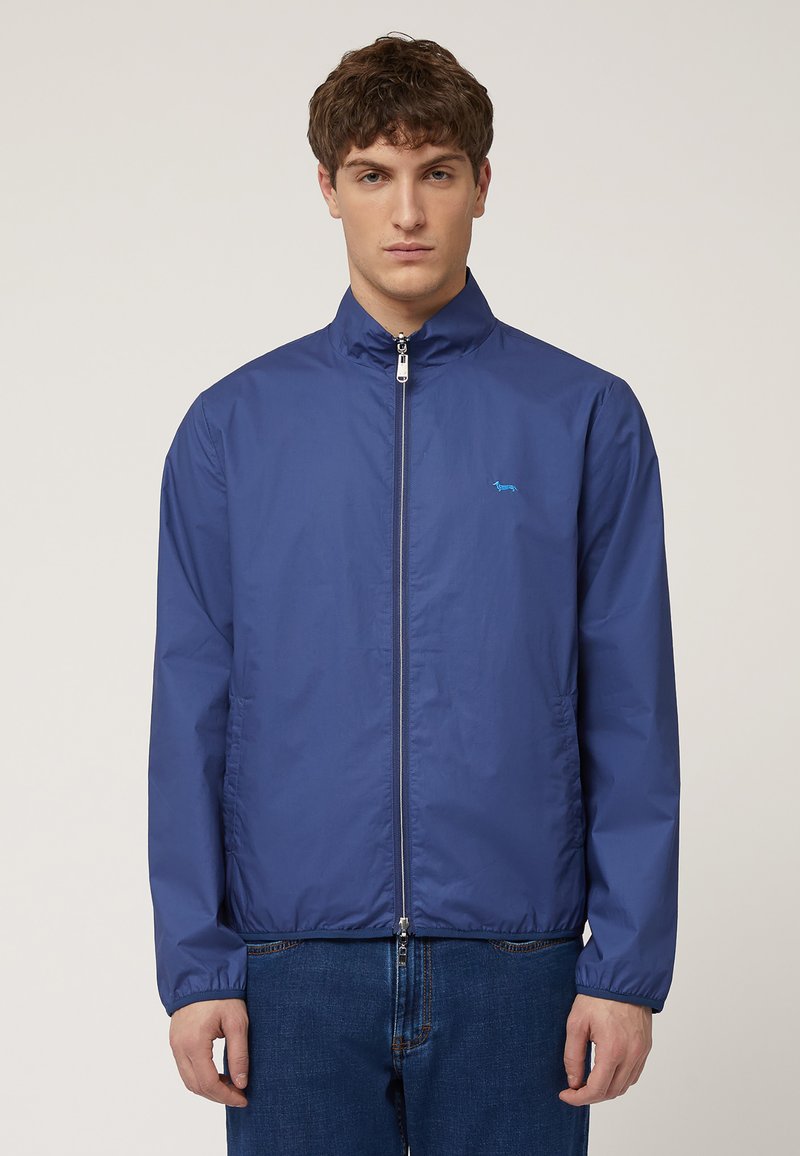 Blå lättvikts zip-up jacka med hög krage, med en liten logotyp på vänster bröst, elastiska ärmslut och en slät textur.
