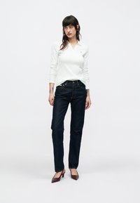 Biele polo tričko s dlhým rukávom, golierom a malým logom, kombinované s tmavomodrými džínsami s rovnými nohavicami a bordovými lodičkami na podpätku.