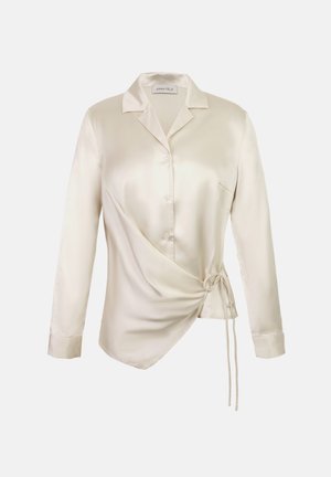Blouse en satin crème avec col, manches longues, fermeture à boutons sur le devant, et un design asymétrique à nouer avec un cordon sur un côté.