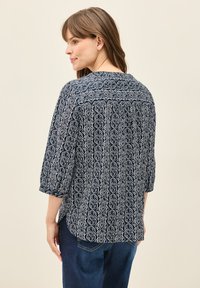Blusa de color navy con intrincados patrones geométricos en blanco, mangas de tres cuartos y un corte holgado con un dobladillo ligeramente curvado.
