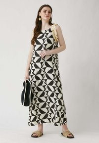 Maxi dress a righe in bianco e nero con spallina gialla arricciata, caratterizzata da una vestibilità morbida e un tessuto liscio. Abbinata a una borsa nera e sandali beige.