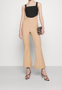 Černý zkrácený top se čtvercovým výstřihem, zkombinovaný s béžovými širokými kalhotami. Modelka drží psaníčko s leopardím potiskem a má na sobě černé sandály na vysokém podpatku.