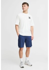 Hvid kortærmet t-shirt med en sort grafik på brystet, parret med marineblå cargo shorts med sidelommer og en afslappet pasform.