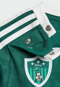 Grüner und weißer Jackenkragen mit Druckknöpfen, weißen Streifen und einem Schild-Patch mit Goofy und drei Sternen über dem Disney-Logo.