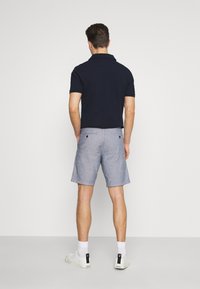 Polo shirt navy associé à un short bleu clair, arrivant jusqu'aux genoux. Le short a un tissu texturé avec deux poches arrière. Des baskets blanches complètent le look.