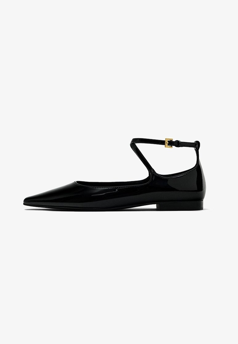 Chaussure plate en cuir verni noir avec bout pointu et fine bride à la cheville avec une petite boucle dorée.