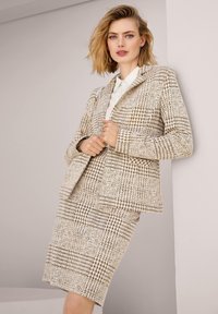 Tweed blazer en rok set in een beige en bruine houndstooth patroon. Kenmerkt zich door een gestructureerd ontwerp, notch revers en een gladde textuur.