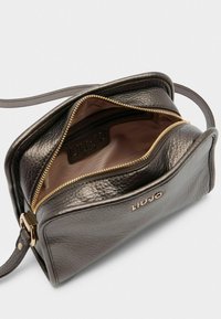 Sac en cuir gris foncé à bandoulière, avec une finition texturée, une fermeture éclair dorée et un intérieur doublé de tissu avec un patch logo.