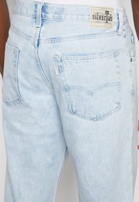 Ljust blå denimjeans med avslappnad passform, femficksdesign och en vintage etikett som säger "silverTab" på bakdelen av midjan.
