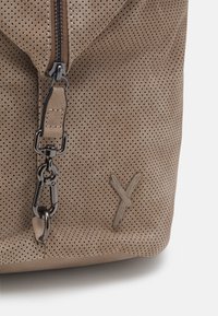 Borsa in pelle beige perforata con chiusura a zip, dotata di un gancio in metallo nero e un dettaglio decorativo a punto X sulla parte frontale.