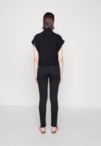 Black knitted sweater with short sleeves and high neck, paired with black fitted jeans. Model wears pink sandals. Background is plain white.