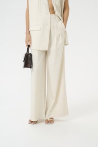 Pantaloni a gamba larga color crema realizzati in tessuto leggero, con pieghe e tasche laterali, abbinati a una borsa a tracolla nera con una forma strutturata.