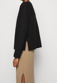 Maglione nero a maglia con una vestibilità ampia, maniche larghe e spalle con fessure laterali, abbinato a una gonna beige con uno spacco fino alla coscia.