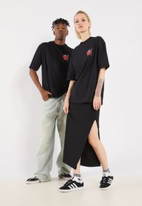 To personer bærer sorte t-shirts, den ene med en høj-slids sort nederdel og den anden med lyseblå jeans, begge i sneakers.
