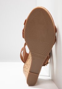Sandale compensée marron avec texture en liège et semelle en caoutchouc. Présente plusieurs brides et une boucle ajustable. Taille 37 visible sur la semelle.