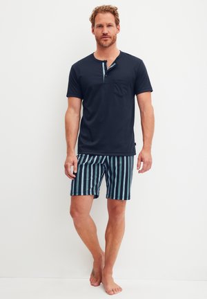 Marineblauw T-shirt met korte mouwen, een zakje en knoopdetail; gecombineerd met gestreepte zwemshorts in donkerblauw, groen en wit.