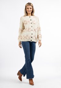 Cardigan chunky in crema con morbide strisce corallo, dotato di grandi bottoni marroni, polsini a costine e una vestibilità rilassata. Abbinato a jeans svasati.