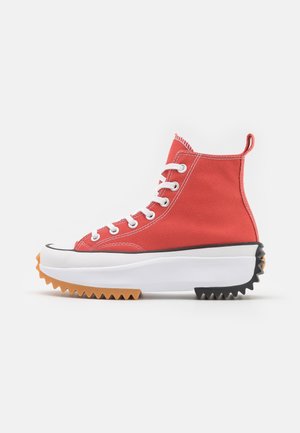 High-top red canvas sneaker with white laces, thick white sole, and serrated gum and black rubber outsole.