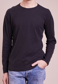 Long-sleeve black cotton shirt with a crew neckline, featuring a smooth texture and casual fit, paired with blue distressed jeans.