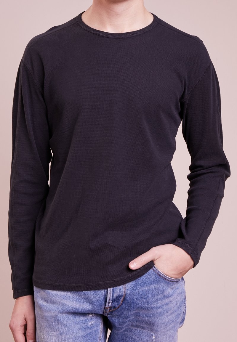 Long-sleeve black cotton shirt with a crew neckline, featuring a smooth texture and casual fit, paired with blue distressed jeans.