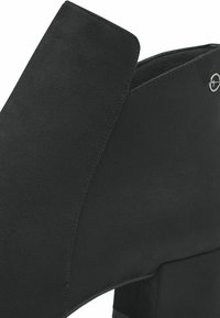 Bottines noires en daim avec un talon carré, présentant une texture lisse, une coupe angle et un petit logo circulaire.