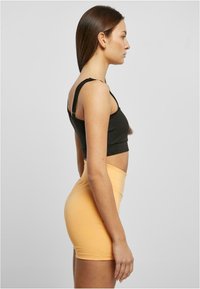 Fekete crop top állítható pántokkal, amelyet egy testhez simuló, magas derekú világos narancssárga mini szoknyával párosítottak, kiemelve a sima textúrát és az elegáns formatervezést.
