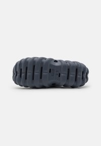 Mörkgrå skor tillverkade av texturerat material, med en ruggad, rundad design och ventilationshål för andningsförmåga.