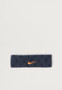 Námořnická látková čelenka s prošívanou texturou, s oranžovým logem Nike swoosh. Má elastický, přiléhavý design pro pohodlí.