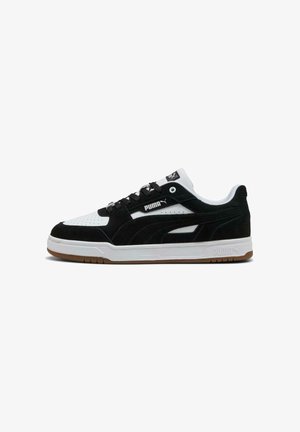 Low-top Puma sneaker in black and white suede with perforated toe, black laces, white sole, and brown rubber outsole, side logo visible.