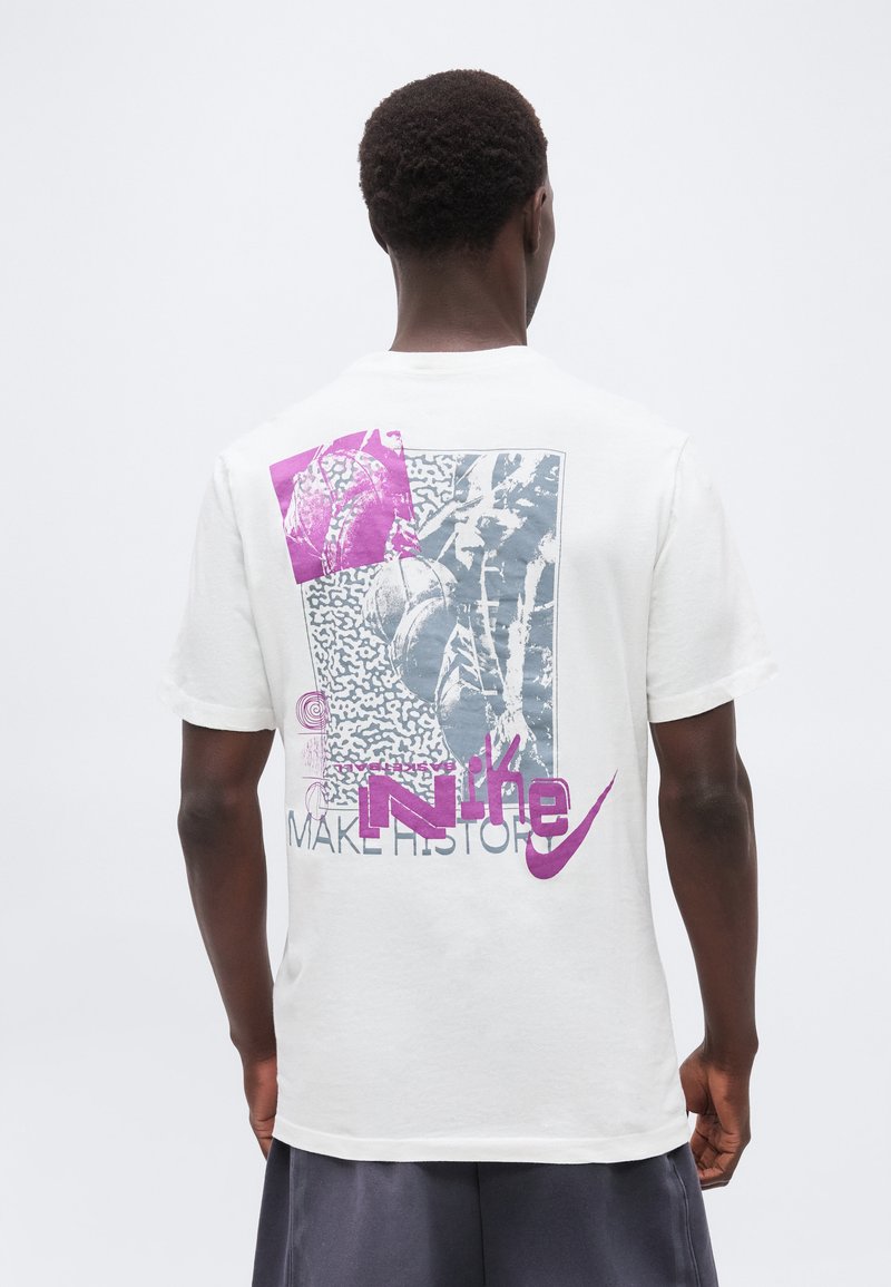 Άνδρας με την πλάτη φοράει λευκό T-shirt της Nike με αφηρημένο γκρι και μοβ γραφικό και το κείμενο "MAKE HISTORY" στην πλάτη.