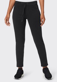 Schwarze Jogginghosen mit Kordelzugbund, enger Passform, seitlichen Taschen und glatter Oberfläche. Kombiniert mit schwarzen Sneakers für einen lässigen Look.