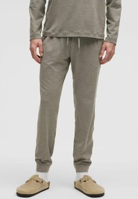 Grå langærmet top og joggers i blødt stof. Bukserne har en elastisk talje med snøre; modellen har beige slip-on sko på.