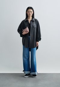 Camisa larga de couro preto, top preto, jeans de cintura alta azul claro, mala rosa. Ténis pretos com sola branca. Texturas suaves, ajuste casual.