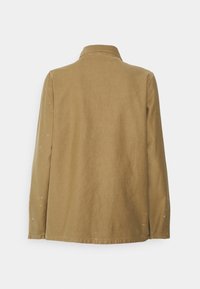 Camisa de algodón color beige con cuello, mangas largas y aberturas laterales. Presenta sutiles manchas de pintura en los hombros y una vista trasera lisa.
