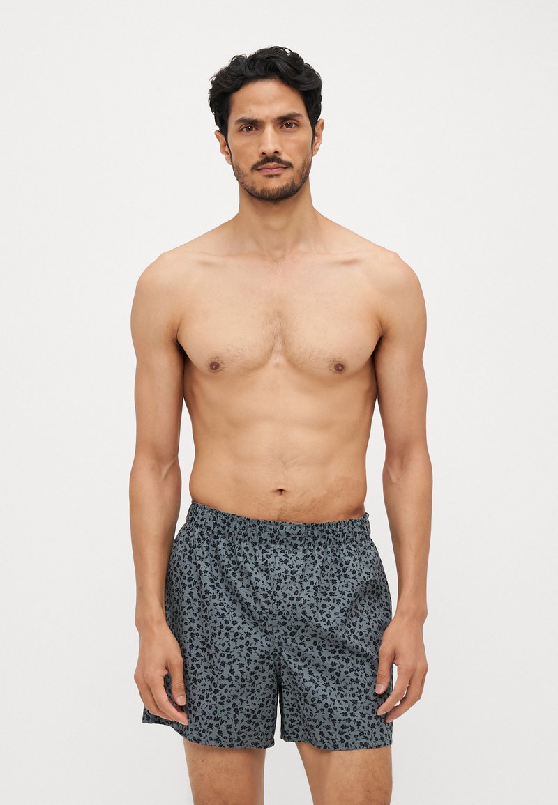 Shorts de bain pour hommes en bleu foncé avec un motif floral. Taille élastique, coupe ample, matériau léger. Texture douce, longueur au-dessus du genou.