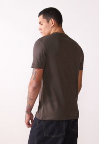 Bruine T-shirt met korte mouwen en een ronde halslijn, gladde textuur en een slanke pasvorm, gecombineerd met donkere denim broek.